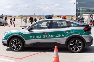 Pojazd Straży Granicznej. W tle podróżni przechodzą do terminala lotniczego. Pojazd Straży Granicznej. W tle podróżni przechodzą do terminala lotniczego.